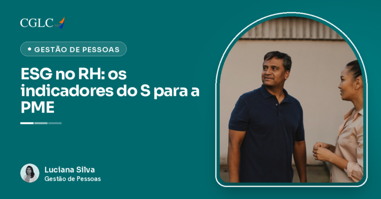 Homem de camisa polo azul-marinho e mulher de camisa bege conversando em pé, virados um para o outro, diante de uma parede clara sob um telhado de telha ondulada. Ele está com a boca entreaberta, olhando para ela, e ela mantém a mão direita fechada na altura da cintura.
