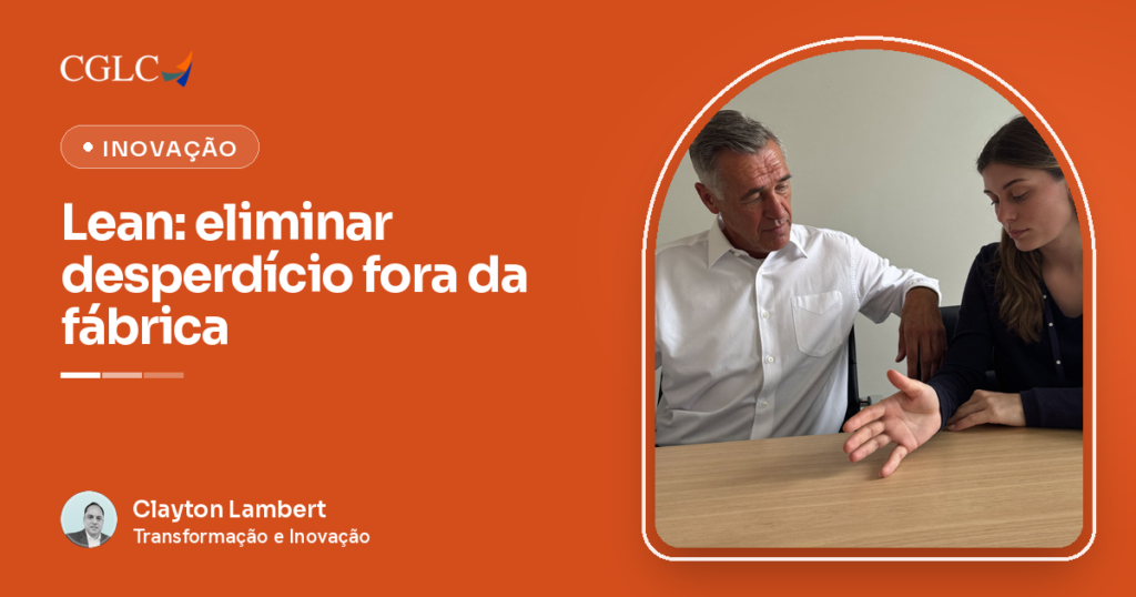 Homem grisalho de camisa branca sentado ao lado de mulher jovem de blusa azul-marinho, os dois olhando juntos para a mesa de madeira clara e vazia à frente, ela explicando com a mão aberta apoiada na mesa.