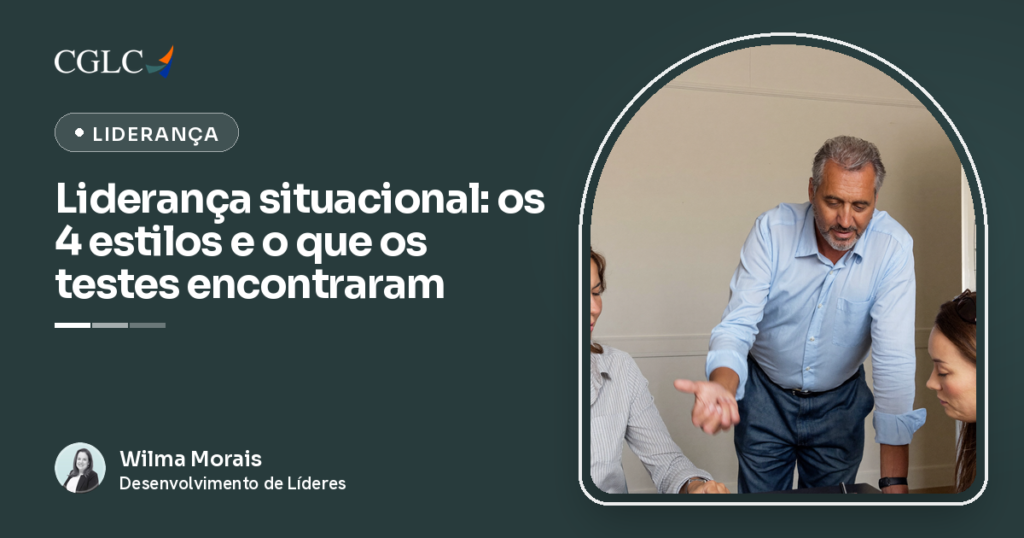 Gestor em pé ao lado de duas profissionais sentadas à mesa, apontando com a mão o próximo passo da tarefa