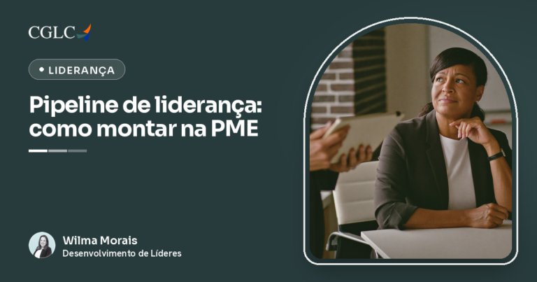Mulher negra de blazer escuro, sentada à mesa de reunião, com a mão no queixo e um leve sorriso, olhando para cima e para o lado, pensativa; à esquerda, o braço de outra pessoa segurando um tablet; ao fundo, parede de tijolos e um quadro branco